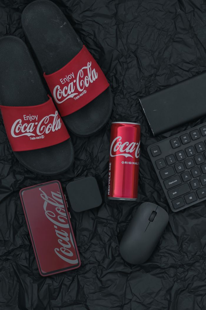The Art of Drawing Readers In: Your attractive post title goes here Flat lay of Coca-Cola themed items including slides, can, and tech accessories on a black background.